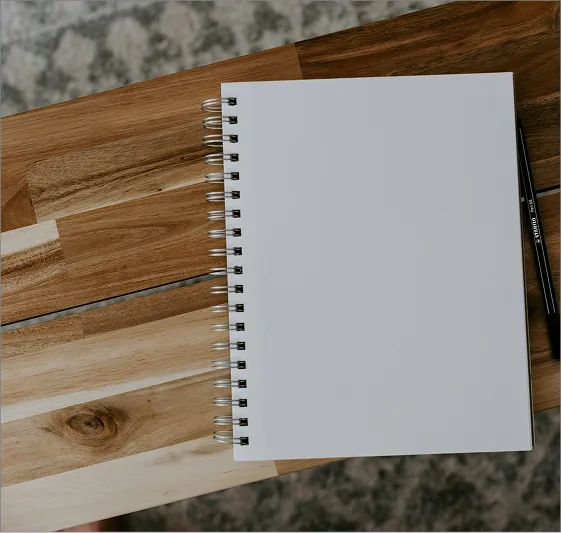 A notepad sitting on top of a wooden table next to a pen.
