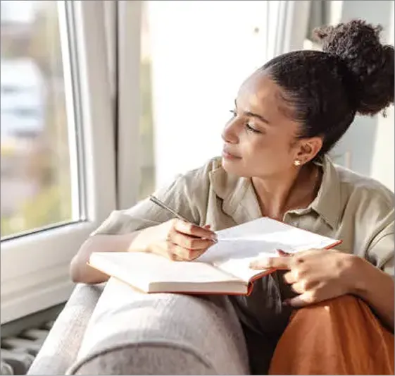 A woman sitting on a couch writing in a book.